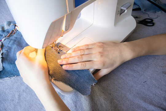 Hands sewing fabric on machine with denim material. DIY clothing repair concept. Sustainable fashion and handmade lifestyle.