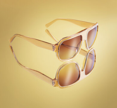 Close up of elegant amber translucent sunglasses reflecting on a golden background
