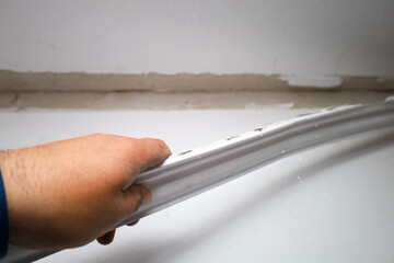 A man's hand is removing or applying a plastic baseboard to the joint between the wall and the ceiling during interior finishing works. The process of cosmetic room renovation, © Олег Струс