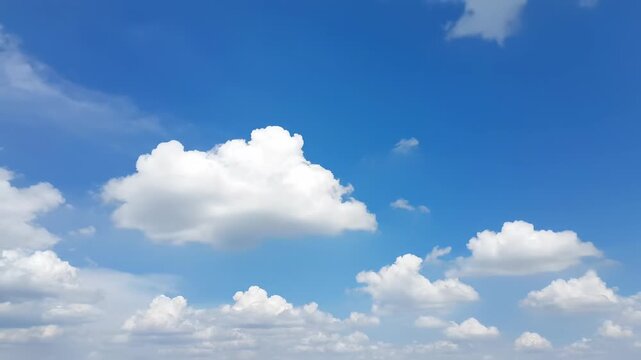 A vibrant blue sky adorned with fluffy, white cumulus clouds. The clouds vary in size and shape, creating a dynamic atmospheric display
