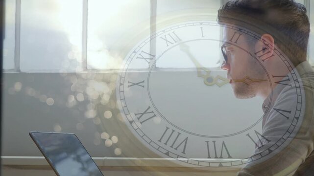 Tech man working on laptop beside window, sunlight rising causing clock hands moving tracking time