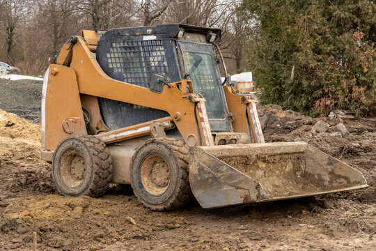 Bobcat excavator performs earthmoving tasks at a construction site on a cold winter day in a rural setting with surrounding trees