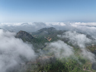 Fototapeta premium Aerial view of lush green mountains surrounded by sea of clouds under blue sky