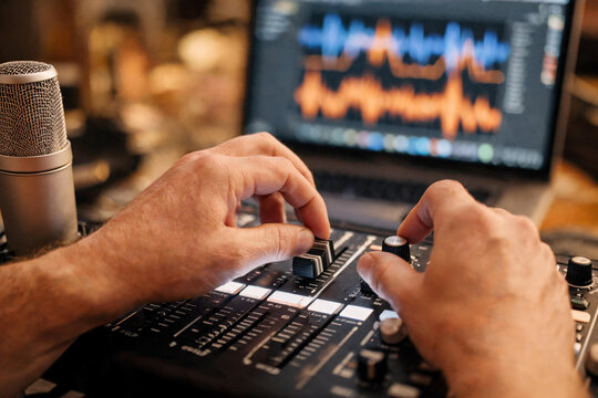 Manos de productor o ingeniero de sonido ajustando los controles de un Ecualizador y faders iluminados de una mesa de mezclas anal&oacute;gica en un estudio de grabaci&oacute;n. 
