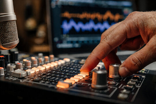 Manos de productor o ingeniero de sonido ajustando los controles de un Ecualizador y faders iluminados de una mesa de mezclas anal&oacute;gica en un estudio de grabaci&oacute;n. 