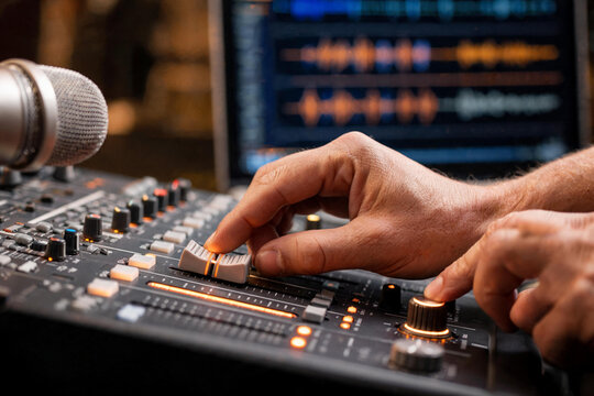 Manos de productor o ingeniero de sonido ajustando los controles de un Ecualizador y faders iluminados de una mesa de mezclas anal&oacute;gica en un estudio de grabaci&oacute;n. 