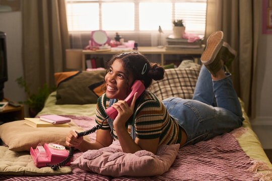 Teenage girl lying on bed and talking on retro landline phone, expressing friendship and nostalgic communication. Ideal for youth lifestyle, teen culture, social connection marketing