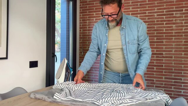 Man prepares to iron a striped shirt, arranging it on the ironing board for a neat and presentable look.