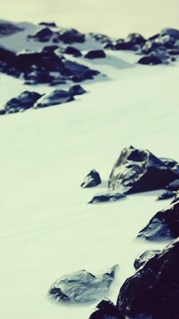 Snow covers the ground in a rocky area with large stones visible. The setting is on a mountain slope. The weather suggests winter with cold temperatures.