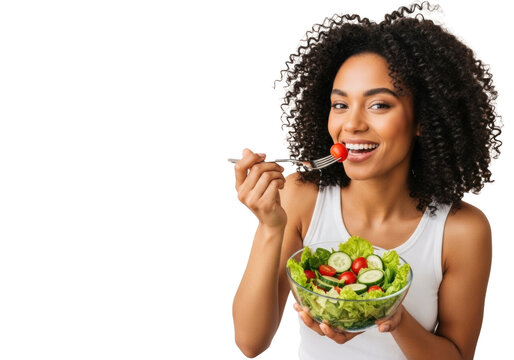 Smiling young african american woman, curly hair, white tank, holding green salad, fork with tomato, bright studio, beige background, copy space, healthy eating wellness concept