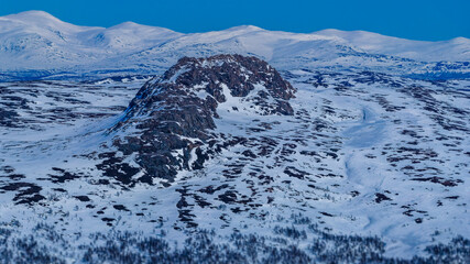 Atoklinten mountain standing prominently in a vast, snow covered winter landscape, presenting a rugged arctic wilderness in Lapland under a clear blue sky © Alexandre Patchine