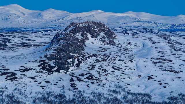 Atoklinten mountain standing prominently in a vast, snow covered winter landscape, presenting a rugged arctic wilderness in Lapland under a clear blue sky