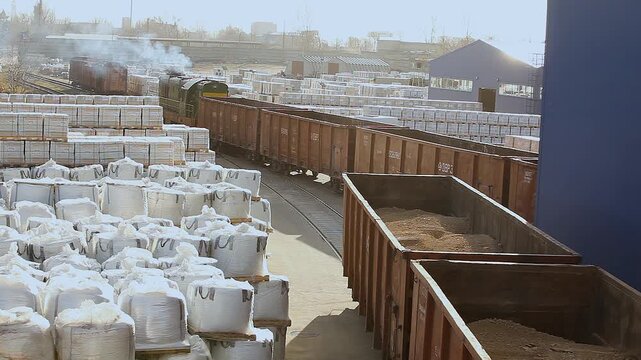 An open freight car loaded with bulk materials moves through an outdoor factory warehouse. Industrial rail freight transportation. Freight railroad transportation.