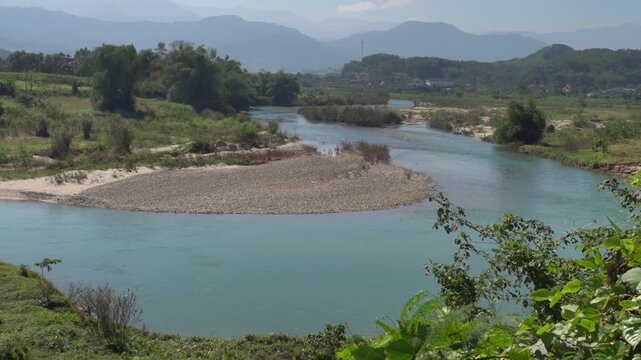 A mountain river with standing water at the outlet of the plain. Pebble and mudflats at low water period. Secondary rain forests and shores are occupied by plantations. Thailand.