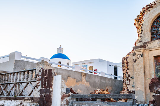 Blue dome church behind rustic ruins in Oia