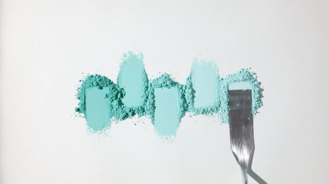 Top angle shot of five cyan shades of smeared powder heaps organized in a row, one smeared with a palette knife on a light gray background