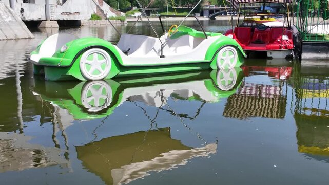 Vintage car shaped pedal boat floating on a park pond with water reflection