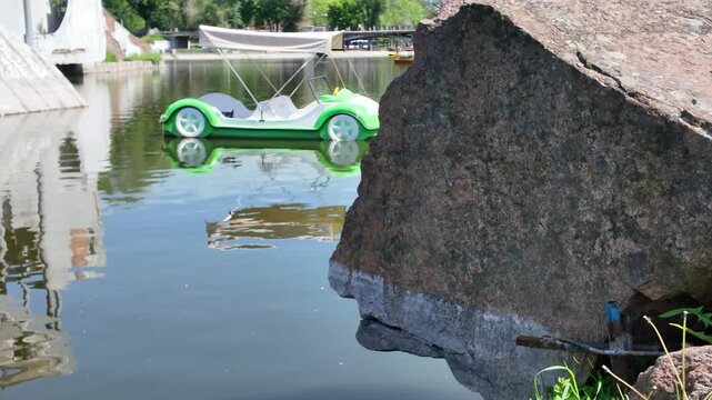 Vintage car shaped pedal boat floating on a park pond with water reflection