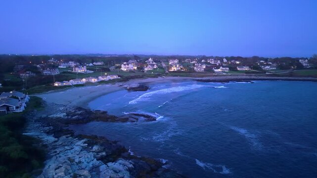 Newport rocky coastline at dusk, a high-angle aerial drone video capturing deep blue ocean waves rolling against a rugged stone shore and luxury seaside estates in Newport, Rhode Island.