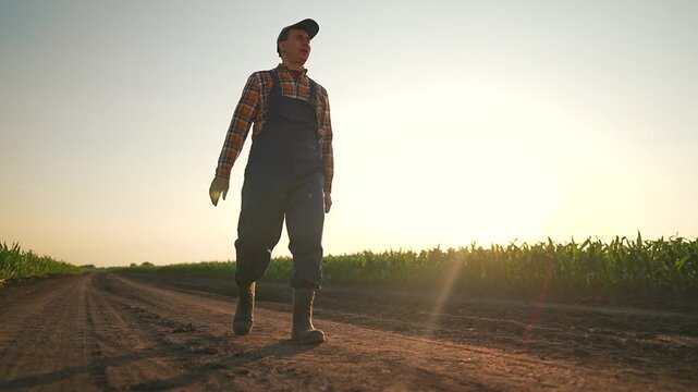 Dirt path curves near wide field. Farmer in strong boots walks slowly by growing corn. Boots tap dirt leaving prints. Path under sunset guides farmer ahead. Field rustles calm. Boots gather dust.