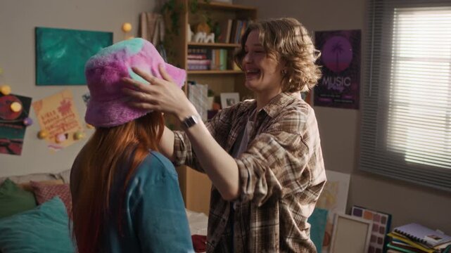 Medium shot of two young Caucasian female friends laughing while trying on funny vintage Y2K outfits in cozy bedroom at home