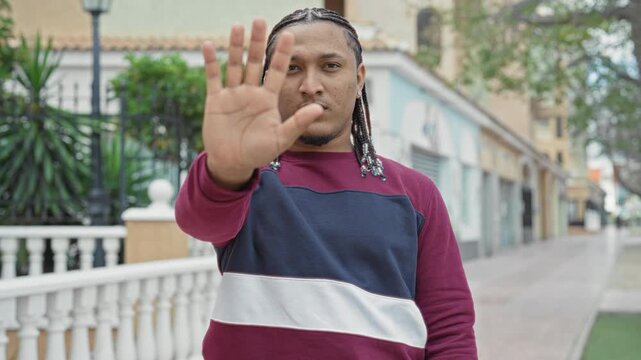 Man with outstretched palm showing stop gesture on street near railing and shops; determination boundary.