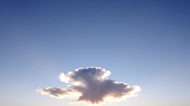 A single fluffy cloud floats in a clear blue sky as the sun sets on the horizon. The backlighting creates a golden glow. Ideal for nature backgrounds or atmospheric transitions.