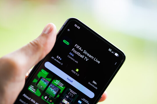 Close-up of a hand holding a smartphone displaying the FIFA+ Stream Live Football TV app on the Google Play Store