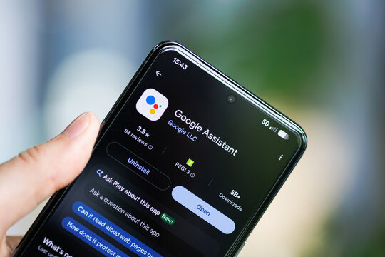 Close-up of a hand holding a smartphone displaying the Google Assistant app on the Google Play Store