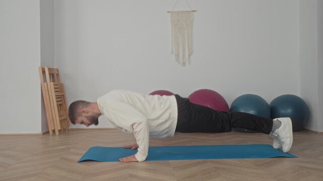 Man performing pushup on a yoga mat with hands grounded and feet extended near exercise balls in studio; strength focus.