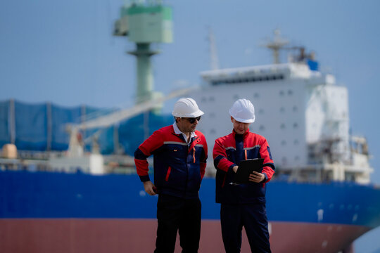 Maritime engineering and cargo logistics concept. Industrial engineers reviewing operational documents and inspection plans at commercial shipping port terminal