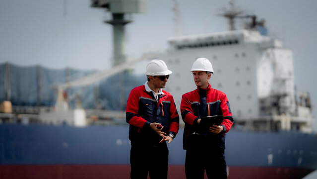 Maritime engineering and cargo logistics concept. Industrial engineers reviewing operational documents and inspection plans at commercial shipping port terminal