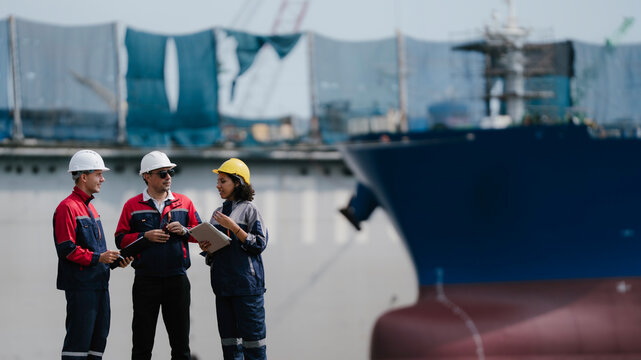 Happy industrial engineering teamwork concept. Smiling maritime engineers collaborating and reviewing project plans at commercial shipping port terminal