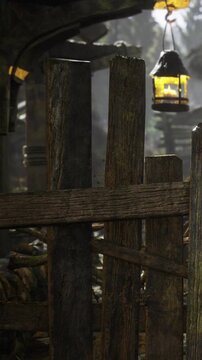 Wooden posts stand in a broken down structure surrounded by greenery. Light filters through the gaps, highlighting parts of the rough wood. Nature is reclaiming the area over time.