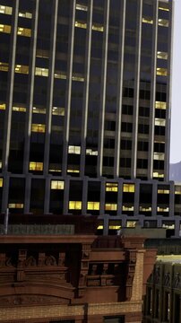 Tall buildings stand against a dusk sky. Some windows are lit while others are dark. The scene shows a mix of modern and older architecture in an urban area.