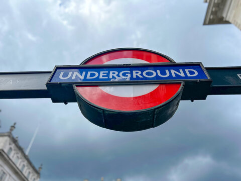 Low-angle view of the iconic red, white, and blue London Underground roundel sign against a cloudy dramatic sky