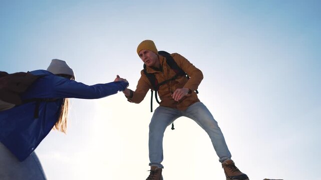 Hiker helps woman climb mountain rock. Man assists partner during outdoor hiking adventure. Couple shows teamwork while climbing. Hikers with backpacks support each other on mountain trail.