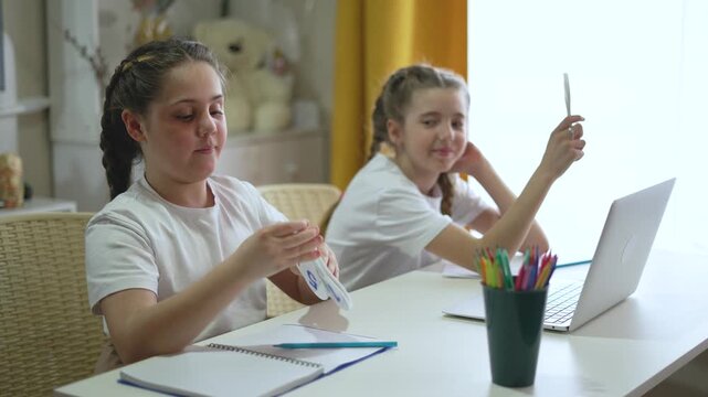 Two girls studying together at home desk with number flashcards smartphone laptop. Sisters learn math online during remote education. Girls practice numbers. Students studying at home desk.