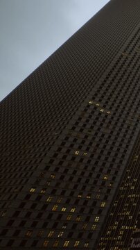 The scene shows a tall building captured from below during the evening. Some windows are lit, indicating people are present inside. The sky is dim, adding to the urban atmosphere.