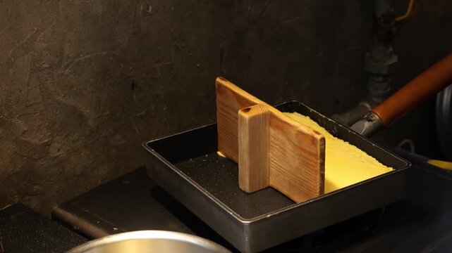 Close-up of a chef expertly crafting tamagoyaki, a traditional Japanese rolled omelette, in a specialized rectangular copper pan. The footage captures the process of layering and rolling the seasoned 