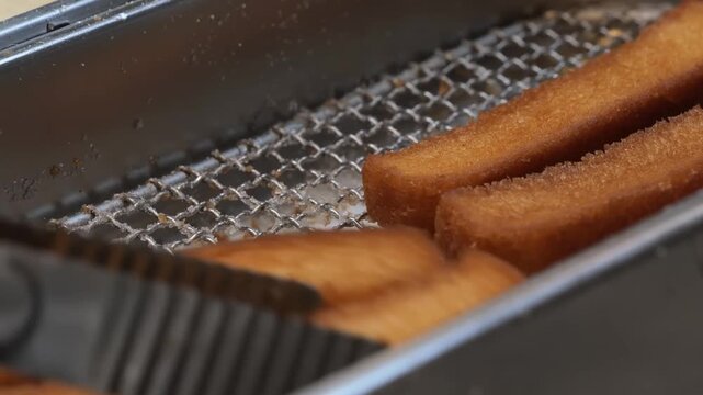 close-up shot of crispy, golden-brown churros resting in a metal fryer basket, showcasing their ridged texture and fresh-fried appearance.