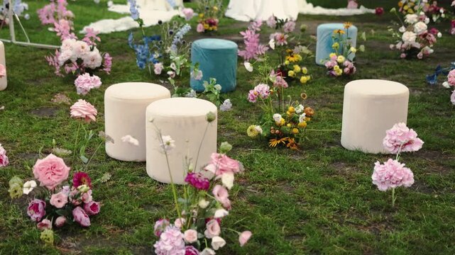 Wedding seating setup with elegant poufs and flower decor on grass for outdoor ceremony in 4k slow motion. Luxury lounge zone arrangements, marriage venue garden party layout.