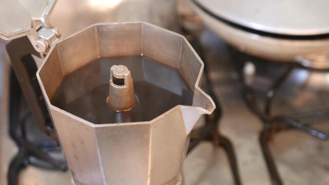 Close-up of a moka pot on the stove. Hot coffee steam rising intensely from a coffee maker. Black coffee in an Italian coffee maker. POV: making espresso. Brewing coffee. Drinking coffee. A hot drink