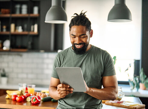 Happy young man having fun preparing food and looking for recipes online using a tablet in kitchen, or a young businessman working from home office making connections online