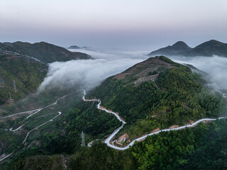 Fototapeta premium Aerial view of winding mountain road surrounded by sea of clouds and lush green forests