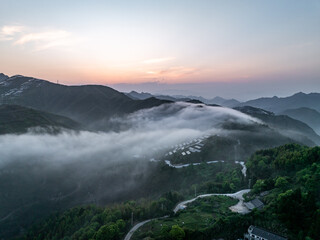 Fototapeta premium Winding mountain road through lush green hills covered in morning clouds and mist
