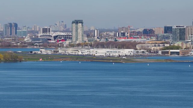 Aircrafts taxiing at Billy Bishop Toronto City Airport showing modern high rise architecture and Lake Ontario on a clear sunny spring day