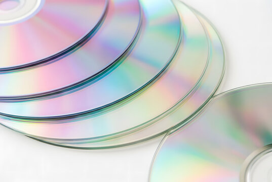 Stack of shiny compact discs reflecting iridescent colors on white background.