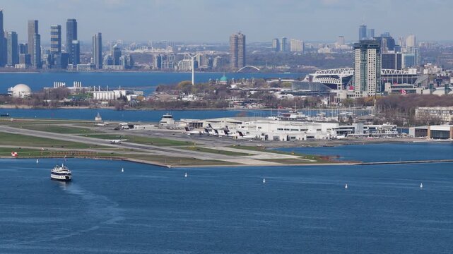 Ferry arriving at Billy Bishop Toronto City Airport with aircraft taxiing, skyline featuring Exhibition Place, Ontario Place, Rogers Centre, urban transportation