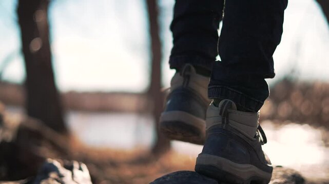 Hiker walking on forest trail wearing hiking boots during outdoor adventure. Person steps on rocky path with boot footwear. Trekking shoes move along nature trail. Hiker explores wilderness terrain.